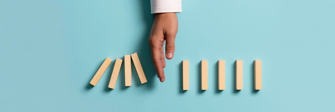 Hand stopping falling dominoes as a business strategy for crisis management and risk prevention