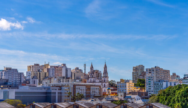 Detailed view of historic and modern downtown urban skyline featuring church spires and high-rise office buildings set against a bright blue sky with light clouds in Porto Alegre, Brazil