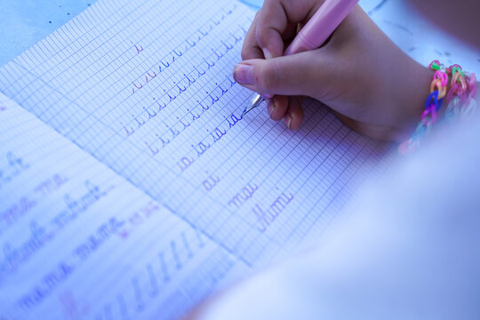 Close-up of a young pupil practicing cursive handwriting with a classic fountain pen in a lined school notebook, developing literacy skills in classroom.