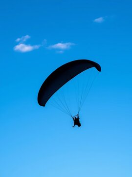 Silhouette of a paraglider in flight against a blue sky with a hint of cloud, adventure, rush
