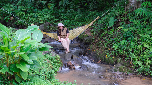 A woman sitting and relaxing in wooden hammock in the creek