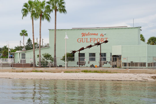 Pastel green waterfront building with a large 'Welcome to Gulfport' sign, palm trees and a sandy shoreline beside a public pier. Editorial Use Only October 3, 2026 Gulfport, FL USA evoking coastal sma