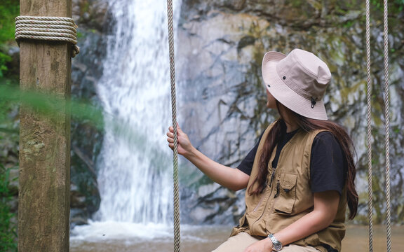 Rear view of a woman sitting and relaxing on swing by the waterfall in the forest
