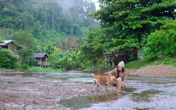 A woman playing with a dog by the river in rural village