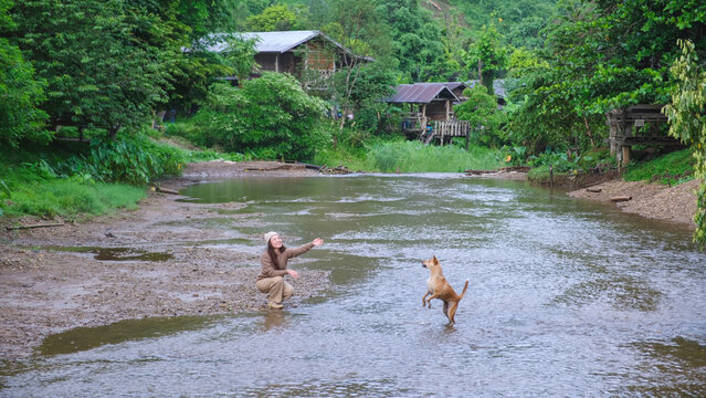 A woman playing with a dog by the river in rural village