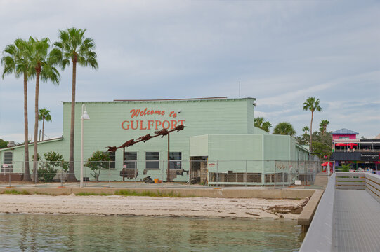 Pastel green waterfront building with a large 'Welcome to Gulfport' sign, palm trees and a sandy shoreline beside a public pier. Editorial Use Only October 3, 2026 Gulfport, FL USA evoking coastal sma