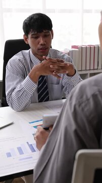 Asian businessman analyzing financial data during a serious business meeting. Man looking worried and stressed while reviewing reports.