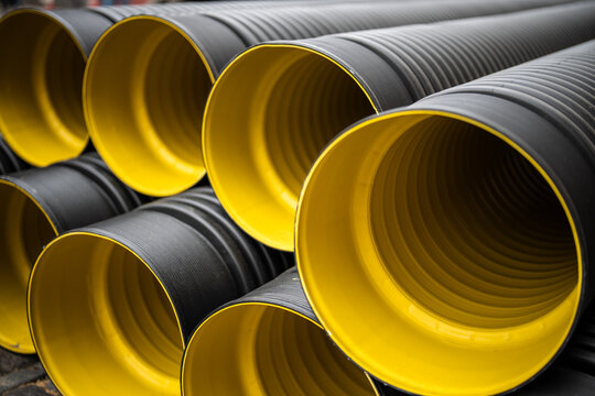 Major maintenance and repairs in urban city, plastic water PVC pipes stacked on ground, bunch of round corrugated tubes ready for installing at construction site, renewal of plumbing systems in town.