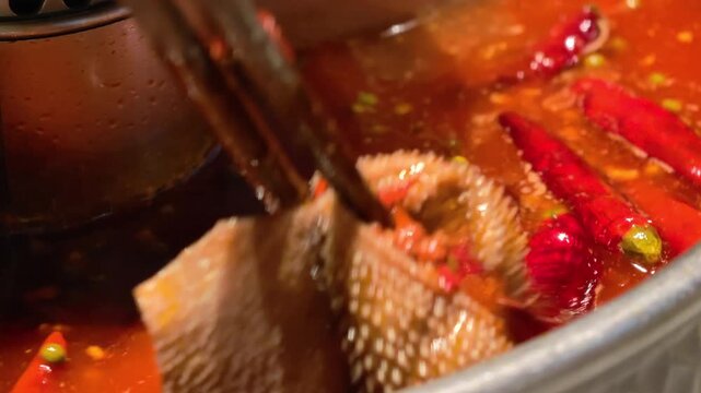 Close-up Chongqing tripe hot pot featuring boiling red chili oil soup base and beef tripe