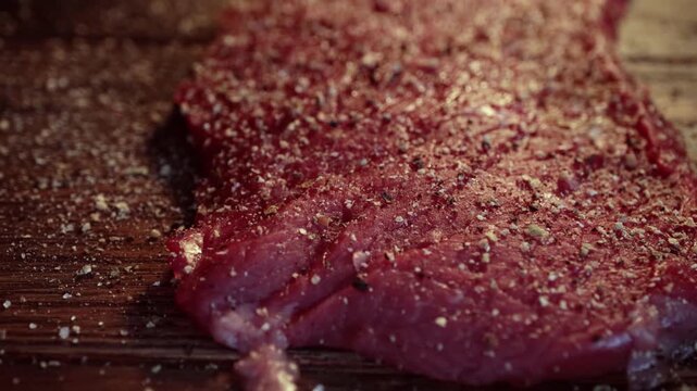 Raw beef steak seasoned with spices and salt on a rustic wooden table for cinematic food preparation footage.