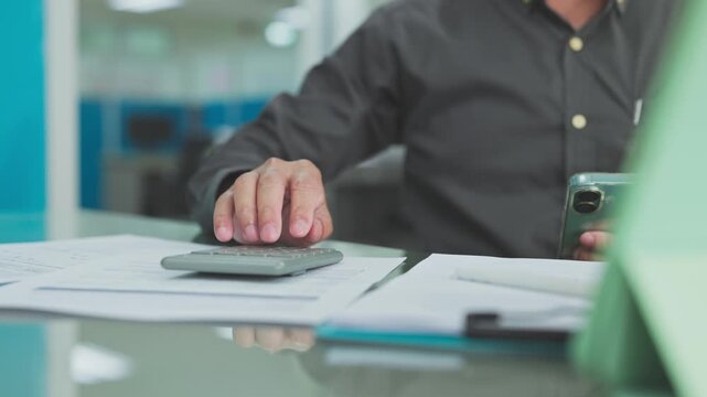 Accountant conducts financial accounting review on paper documents, performing budget accounting analysis with calculator keys.