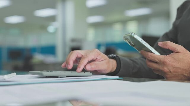 Accountant conducts accounting analysis on desk paperwork, operating mobile phone during audit process complete tax analysis.