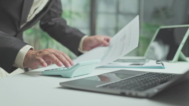 Accountant conducts financial audit duties beside laptop, calculating audit metrics, reviewing tax statement sheets meticulously.