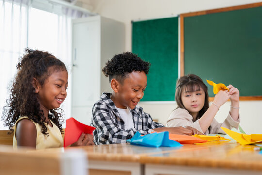 Diverse elementary students folding paper in classroom, multiethnic school children playing with origami and paper craft in class, kids learning and having fun together with paper crafts at school