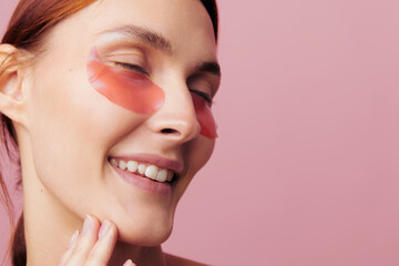 Obraz premium An ecstatic woman smiles with closed eyes, touching her chin in a tight crop. Hydrogel patches under her eyes create a vibrant self-pampering concept for beauty content.