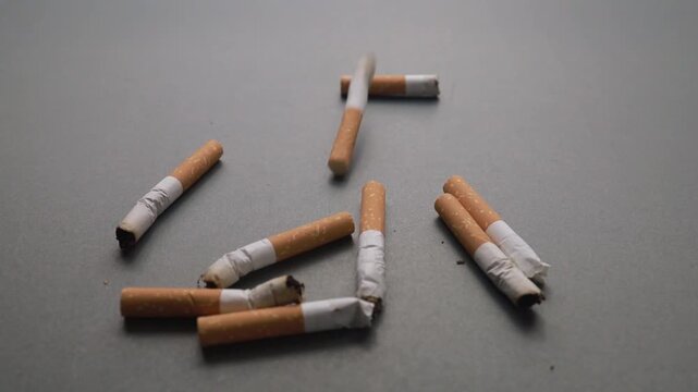 Cigarette butts falling onto a plain grey surface