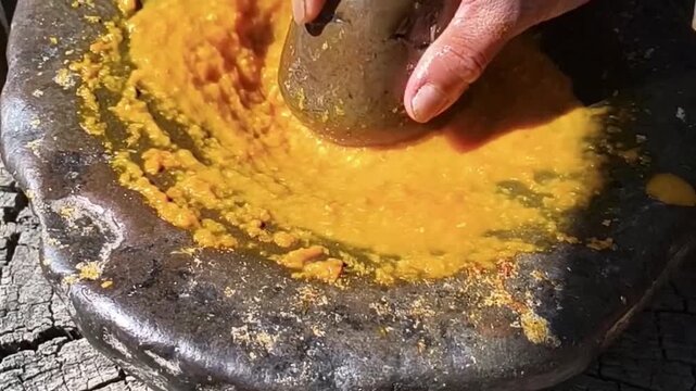Person grinding yellow spices in a traditional stone mortar and pestle