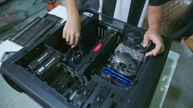 Young boy concentrating while repairing and assembling hardware inside an open desktop computer case at home, learning technology and problem solving skills