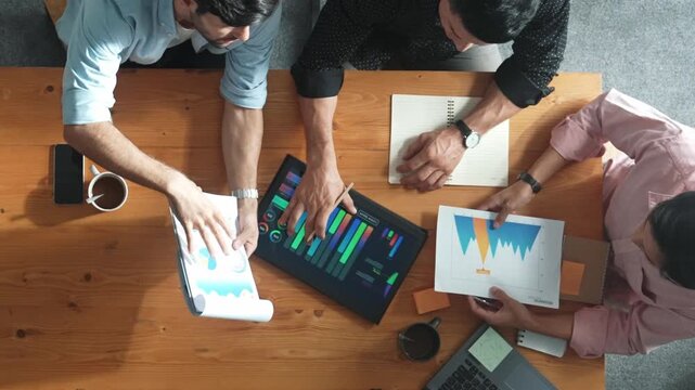 Executive manager explain financial graph to colleague at meeting room. Top aerial view of diverse marketing team sharing idea and planning strategy while sitting at table with tablet. Convocation.