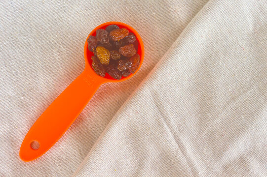 Orange measuring spoon of golden raisins on cotton fabric