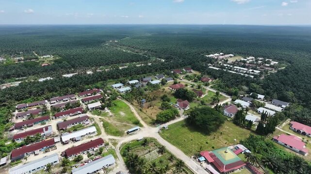 Aerial view of an employee dormitory housing complex for palm oil plantation workers, surrounded by vast green estate fields under a bright sky. Rural communities and agricultural lifestyles.