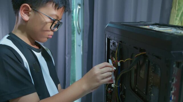 Young boy concentrating while repairing and assembling hardware inside an open desktop computer case at home, learning technology and problem solving skills