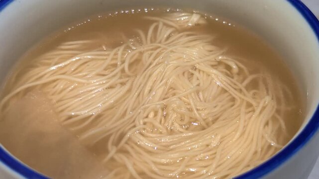 High-angle close-up shot of thin Chinese noodles in clear broth in a bowl	
