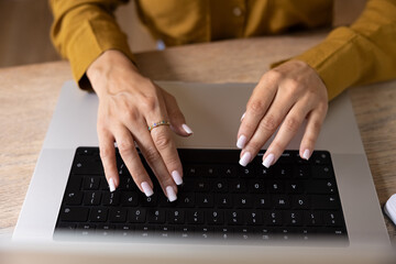 Fototapeta premium Female hands typing on laptop keyboard at office desk, closeup crop view. Businesswoman replying on business email, do remote work, lead digital communication, working online using modern technology