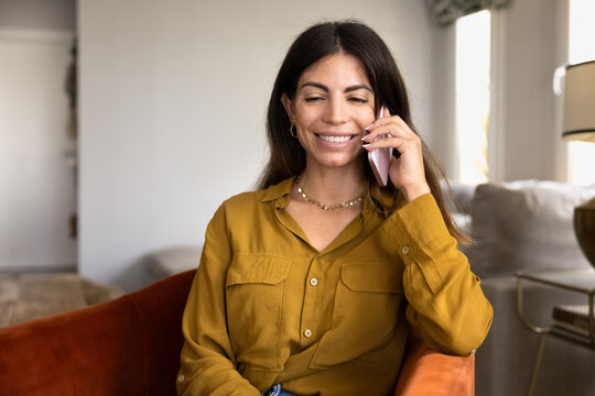 Smiling Hispanic woman having mobile call at home, speaking on smartphone, sharing personal news, enjoying pleasant casual conversation with friend or family. Informal talk, communication, phonecall