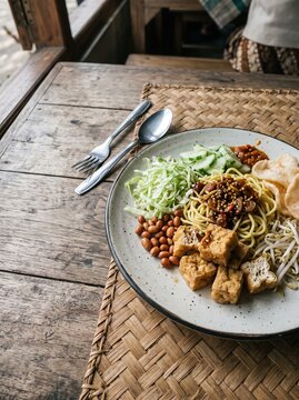 Delicious Indonesian noodle dish with tofu and fresh vegetables on a wooden table.