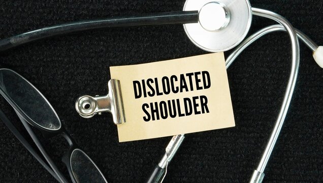 Stethoscope and paper with the words dislocated shoulder happens when the top ball of your upper arm bone pops out of the cup-shaped socket in your shoulder blade.