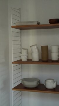 Minimalist wall shelf with ceramic mugs, plates, and a teapot in a modern kitchen
