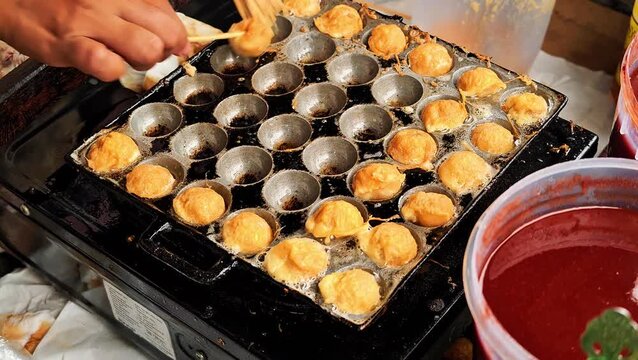 Street vendor cooking fried egg tapioca balls cilor in a special round hole frying pan with bamboo skewers at local market. 4K