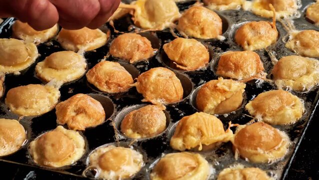 Close up of street food vendor preparing cilor fried tapioca balls with egg in hot oil pan mold using bamboo skewers. 4K