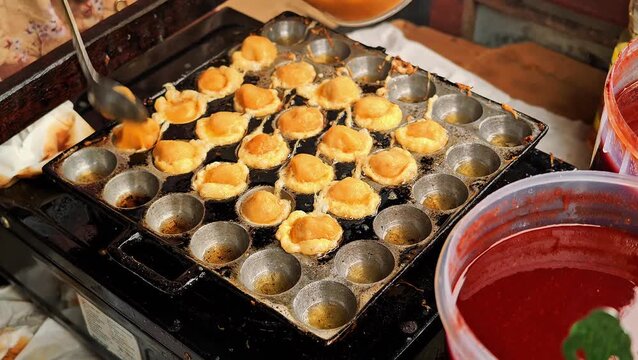 Close up of street food vendor preparing cilor fried tapioca balls with egg in hot oil pan mold using bamboo skewers. 4K