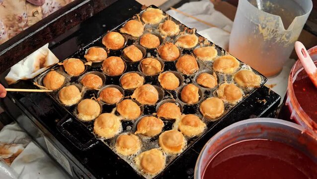 Close up of street food vendor preparing cilor fried tapioca balls with egg in hot oil pan mold using bamboo skewers. 4K