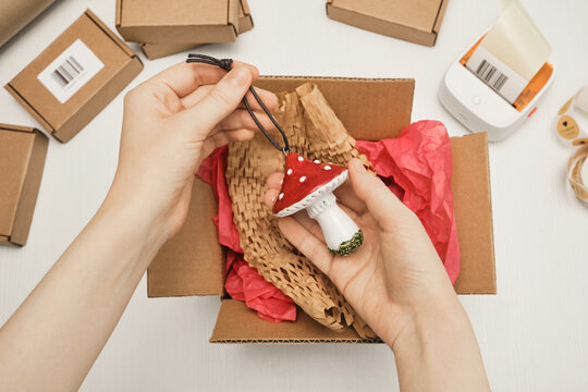 Female Hands packing handmade mushroom ornament in small cardboard box for shipping