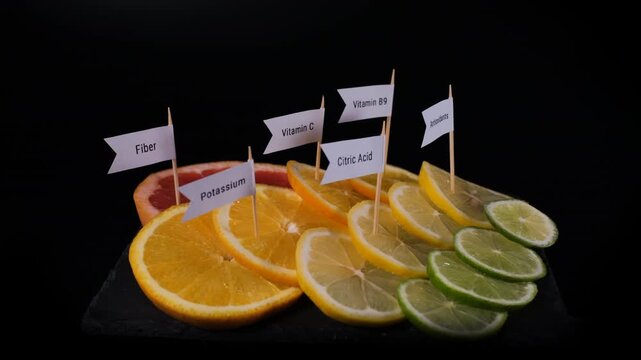 Lime, lemon, orange and grapefruit slices rotate on black slate with potassium, vitamin C, citric acid and antioxidant labels. Fruit nutrition concept