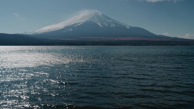 Scenic view of iconic Mount Fuji with snow peak behind Lake Yamanaka under bright blue sky.