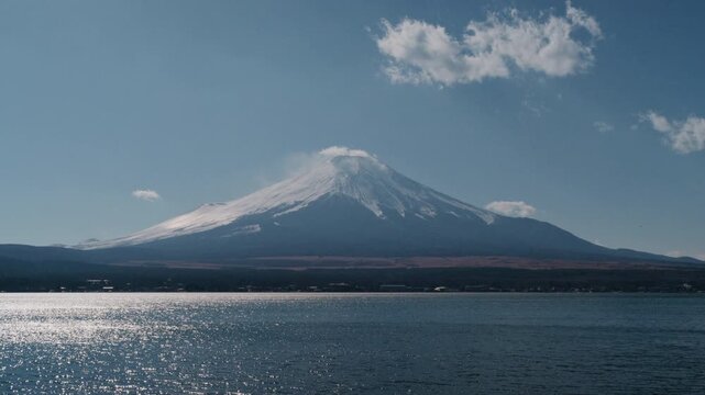 Scenic view of iconic Mount Fuji with snow peak behind Lake Yamanaka under bright blue sky.