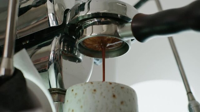 4K Pouring coffee stream from professional machine in cup. Barista man making double espresso, using filter holder. Flowing fresh ground coffee. Drinking roasted black coffee in the morning.	