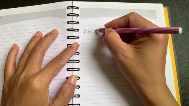 Closeup 4K video showing an unrecognizable person's hand using a black pen to write the words "Profit and Loss" on a blank lined page of a spiral-bound notebook. Clear focus on the handwriting with na