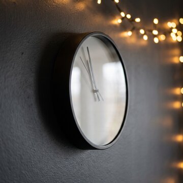 Wall clock showing countdown to midnight with warm fairy lights on dark wall