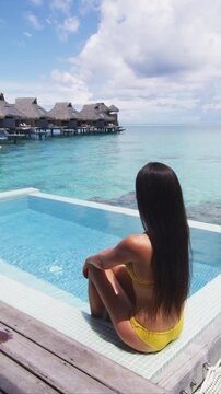 Luxury travel vacation resort destination at idyllic overwater bungalow villa. Woman relaxing by infinity pool. Raw unedited vertical video of real unretouched woman model without any makeup
