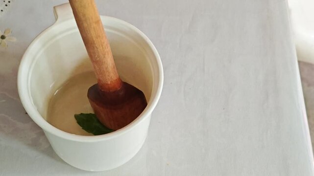 Stirring Fresh Basil Leaves in Cup with Wooden Spoon