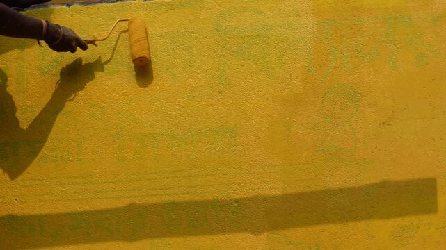 Person painting a textured wall with a yellow roller