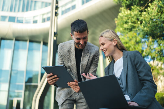 Business colleagues discussing project ideas using digital devices while smiling outside