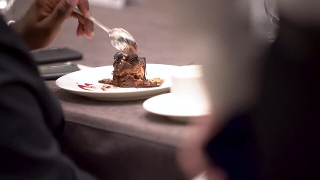 Cinematic close-up video of a hand using a fork to eat a slice of rich chocolate cake in a restaurant setting.

