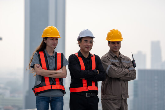 Construction worker group in safety helmet and reflective vest standing confidently at urban building site, teamwork and professional pride expressed against hazy city skyline