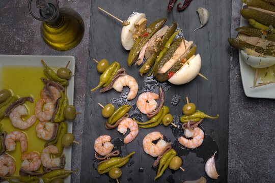 Assortment of traditional Spanish tapas skewers featuring pickles, boiled egg, tuna, olives, anchovies, and prawns served on rectangular plates